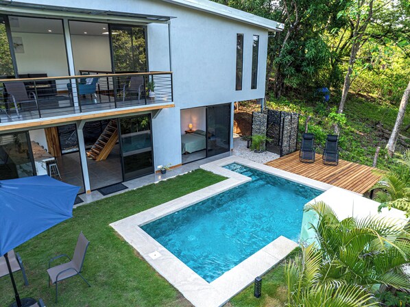 Una casa moderna de dos plantas con piscina, mobiliario de exterior y una escalera que lleva a la planta superior.