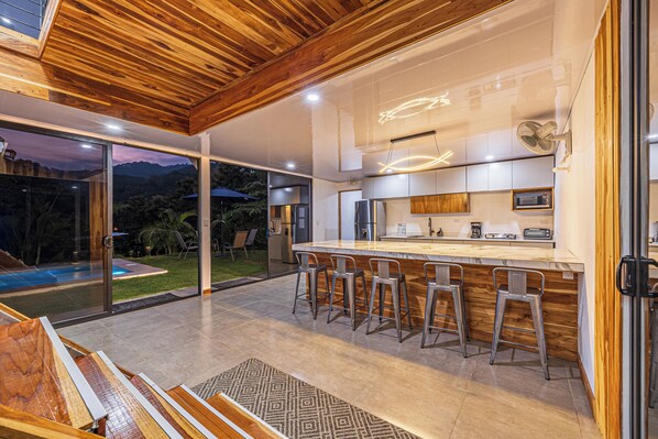 Una cocina moderna con barra, ventanas amplias y una piscina visible al exterior.