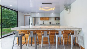 A modern kitchen with a large island, bar stools, and a view of greenery outside. - 3BR - Mountain View - Amazing Pool - 5 min to the Beach - Guanacaste (Puerto Carrillo)