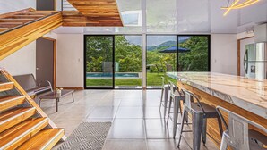 A modern kitchen with a large island, wooden staircase, and a view of a pool and greenery. - 3BR - Mountain View - Amazing Pool - 5 min to the Beach - Guanacaste (Puerto Carrillo)
