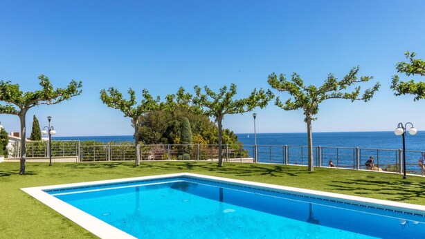 Una piscina rectangular con superficie de agua azul cristalina, rodeada de césped cuidado y una valla de metal.