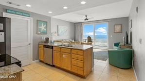 A modern kitchen with wooden cabinets, a large island, and a view of the ocean through the sliding glass doors. - PARADISE FOUND! 2ND FL BEACHFRONT CONDO W/KITCHEN, POOLS, WATERPARK & OTHER FUN! (Panama City Beach)
