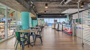 A modern cafe interior with wooden tables and chairs, a counter with a menu, and a view through large windows. - PARADISE FOUND! 2ND FL BEACHFRONT CONDO W/KITCHEN, POOLS, WATERPARK & OTHER FUN! (Panama City Beach)