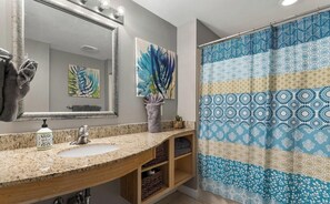 Une salle de bain dotée d’un comptoir en granit, d’un lavabo, d’un miroir et d’un rideau de douche à motifs géométriques.