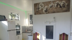 Een compact woongedeelte met een kitchenette, twee stoelen, een bank en een schilderij aan de muur.