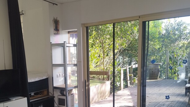 Een moderne keuken met een glazen tafel, houten vloer en een schuifdeur van glas die leidt naar een buitenruimte met een houten terras en begroeiing.