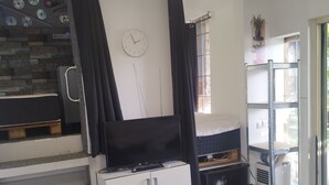 Een ruimtelijk ingerichte leefruimte met kitchenette, een bed, een televisie en een raam met gordijnen.