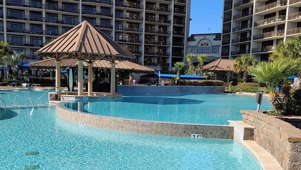 A large outdoor swimming pool with a gazebo, surrounded by high-rise buildings.