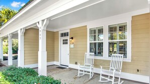 A covered porch with white rocking chairs, beige siding, and a white door.