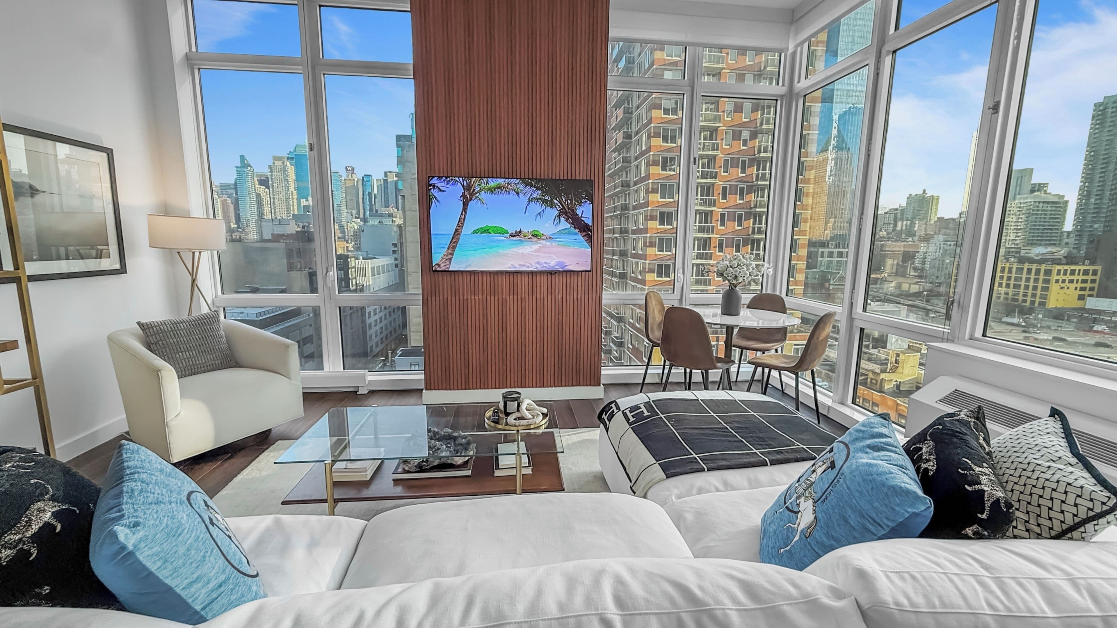 A modern living room with a large TV, comfortable seating, and a city view.