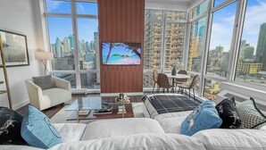 A modern living room with a large TV, comfortable seating, and a city view.