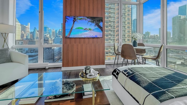A modern living room with a large TV, a glass coffee table, a sofa, and a dining area with chairs.