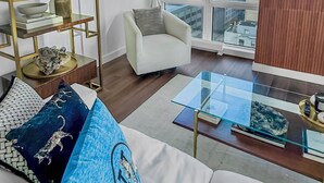 A modern living room with a city view, a white armchair, a glass coffee table, and decorative shelves.