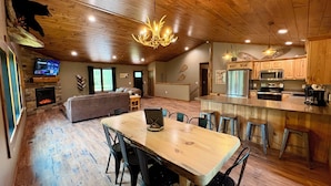 A spacious living area with a fireplace, a large dining table, and a kitchen with modern appliances. - Bear Paw Lodge • Luxury Cabin • Game Room • Fire Pit (Wisconsin Dells)