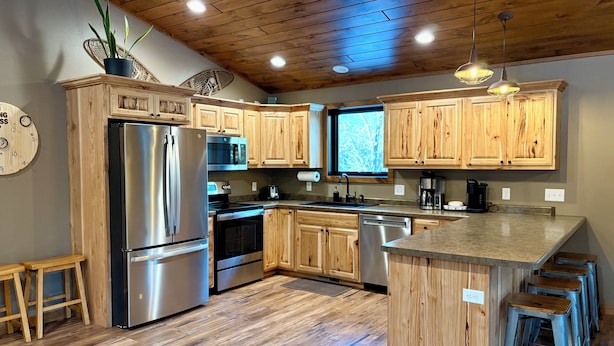 A modern kitchen with wooden cabinets, stainless steel appliances, and a central island with bar stools. - Bear Paw Lodge • Luxury Cabin • Game Room • Fire Pit (Wisconsin Dells)