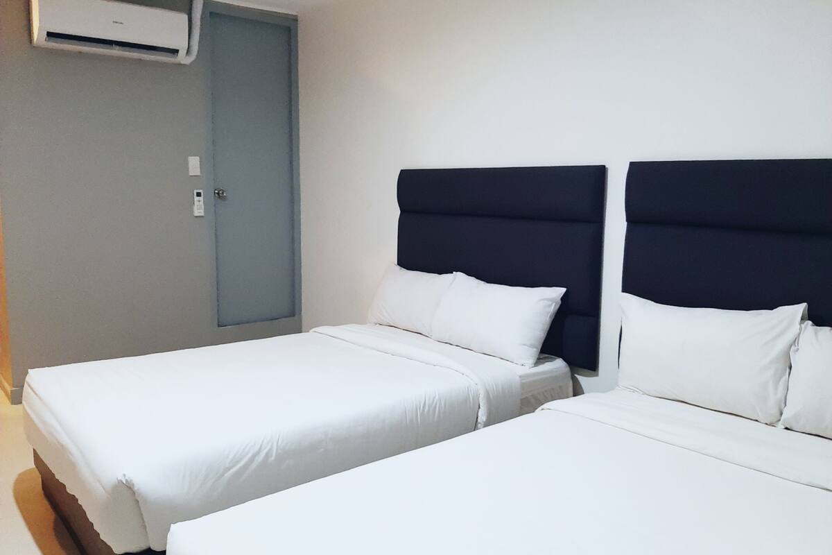 A hotel room with two single beds, a grey door, and a wall-mounted air conditioner.