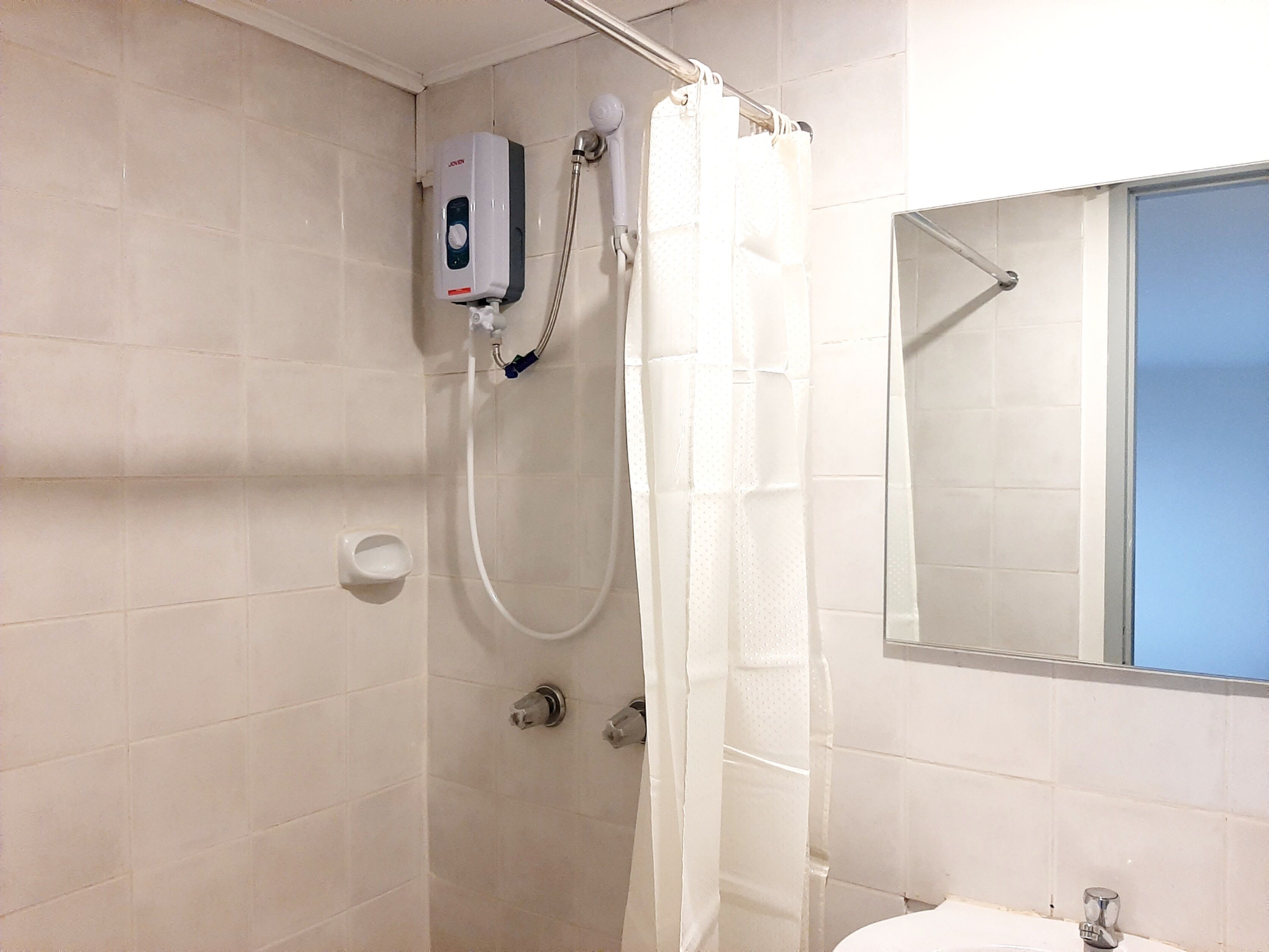 A bathroom with a shower, a hand soap dispenser, and a mirror.