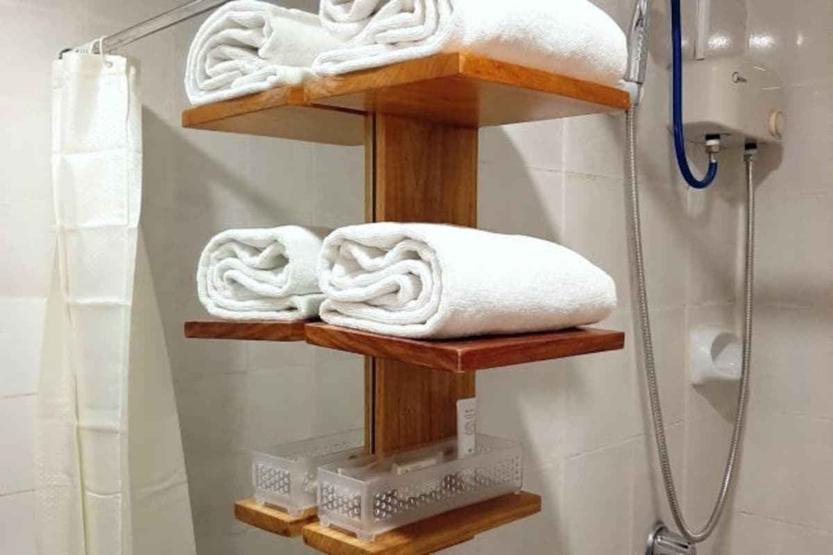 A bathroom with a shower, a towel rack with three towels, and a showerhead.