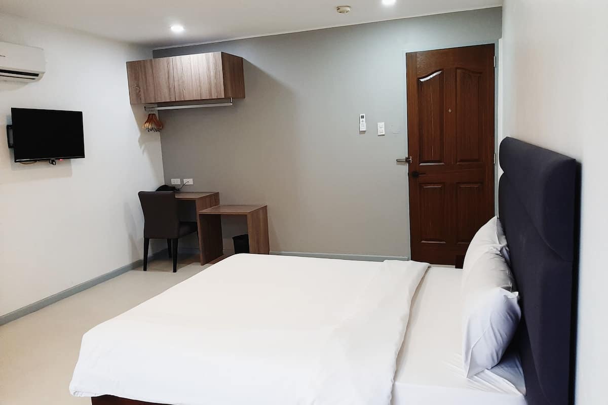 A bedroom with a bed, a desk, a chair, a television, and a wardrobe.