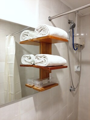 A bathroom with a wooden towel rack holding folded towels, a shower with a handheld showerhead, and a glass shower enclosure. - Anex Hotel-Manila (Manila)