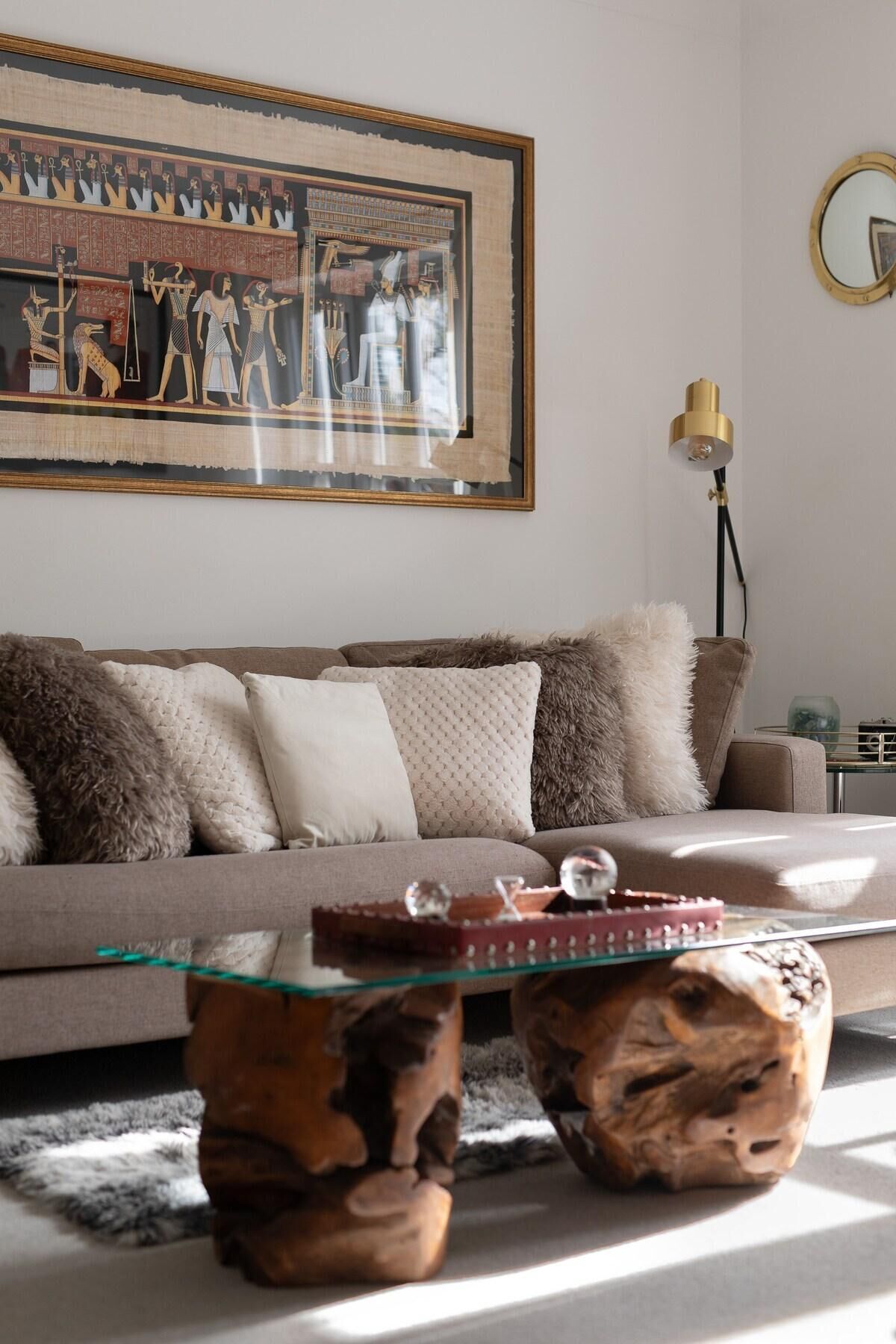 A living room with a sofa, decorative pillows, a glass coffee table, and a framed ancient Egyptian painting.