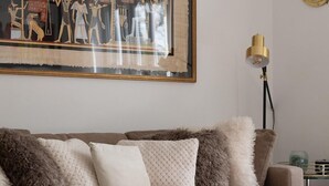 Een woonkamer met een bank, decoratieve kussens, een glazen salontafel en een lijst met een oud-Egyptische schildering.