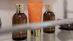 Een badkamer met een spiegel, een wastafel en drie flessen Baylis & Harding Black Pepper Essence.