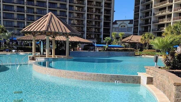 Una piscina con un pabellón, rodeada por un edificio de apartamentos con balcones.