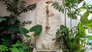 A shower area with a stone wall, surrounded by lush tropical plants. - Gaze Villa by Betterplace (Canggu)