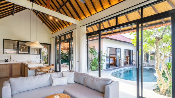 A modern living room with a large gray sofa, a wooden coffee table, and a view of a swimming pool and outdoor area. - Gaze Villa by Betterplace (Canggu)