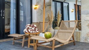 A wooden deck with wicker chairs, a small round table, and a coconut. - Gaze Villa by Betterplace (Canggu)