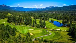 Un parcours de golf avec un lac, entouré de forêts denses et de montagnes.