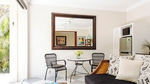 A room with a large mirror, two chairs, a round table with a vase, a sofa with patterned cushions, and a refrigerator. - Beautiful 1 bedroom villa in perfect location (Bali)
