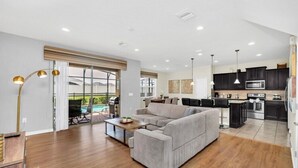A spacious living area with a grey sofa, wooden coffee table, and a large window overlooking a pool.