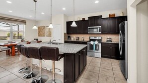 A modern kitchen with dark cabinetry, stainless steel appliances, and a central island with bar stools.