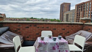 A rooftop terrace with a table set for two, surrounded by brick walls and overlooking a residential area with apartment buildings. - Apartment Sleeps 4 with Free Parking (London)