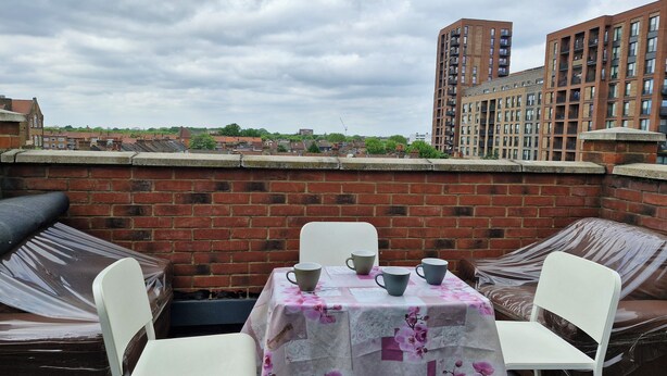 Une terrasse sur le toit, avec une table dressée pour deux, entourée de murs en briques et donnant sur un quartier résidentiel avec des immeubles d’habitation.