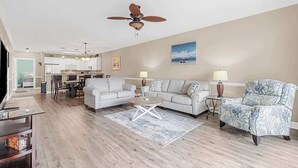Ein geräumiges Wohnzimmer mit Deckenventilator, zwei Sofas, einem Couchtisch und einem Essbereich im Hintergrund.