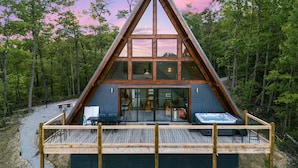 Una cabaña de madera con amplio ventanal, mobiliario exterior y un jacuzzi.