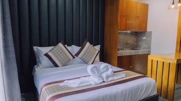 A hotel room with a bed, a wooden wardrobe, a small wooden table, and a modern kitchen area.