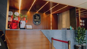 Zona de recepción de un hotel con un mostrador de madera, un cartel que dice "SHINE Boutique Hotel" y una barrera de cuerda roja.