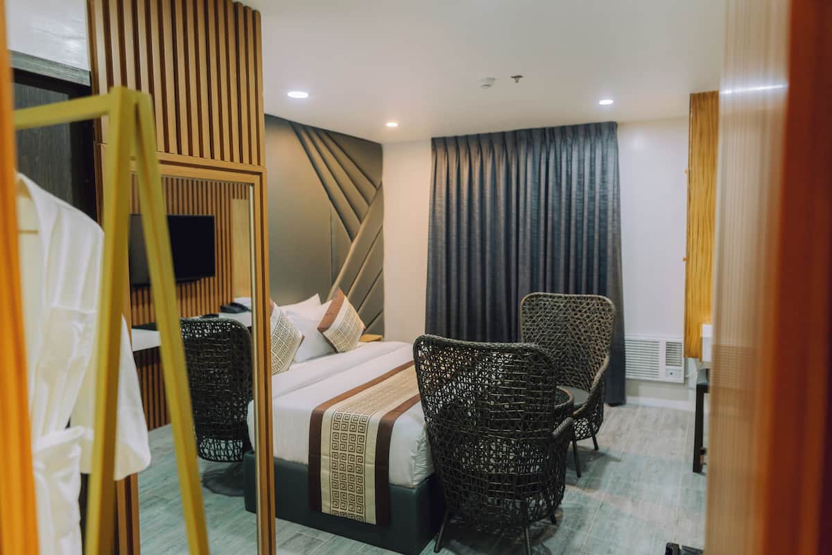 A hotel room with a bed, two wicker chairs, a flat-screen TV, and a large mirror.