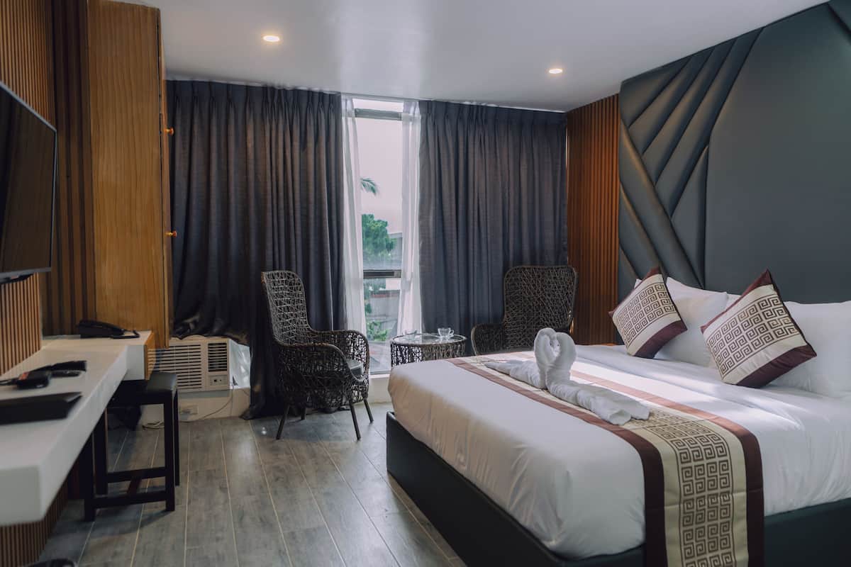 A hotel room with a large bed, a desk, a chair, and a small table.
