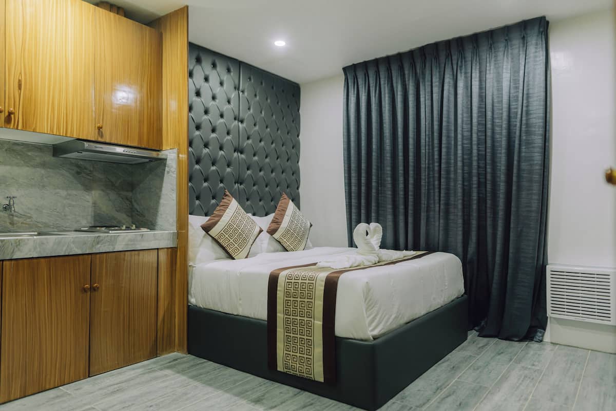 A modern hotel room with a marble countertop, a tufted headboard, a bed with decorative pillows, and a large window with curtains.