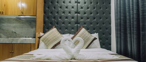 A hotel room with a tufted headboard, a bed with white linens, and a decorative swan towel arrangement.
