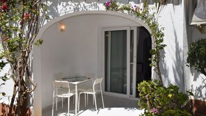 A white outdoor patio with a table and chairs, a sliding glass door, and climbing plants.