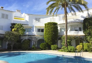 Ein weißes Gebäude mit Pool, Palmen und einem gepflegten Garten.