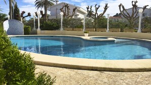 A swimming pool with a curved edge, surrounded by palm trees and a white building in the background.