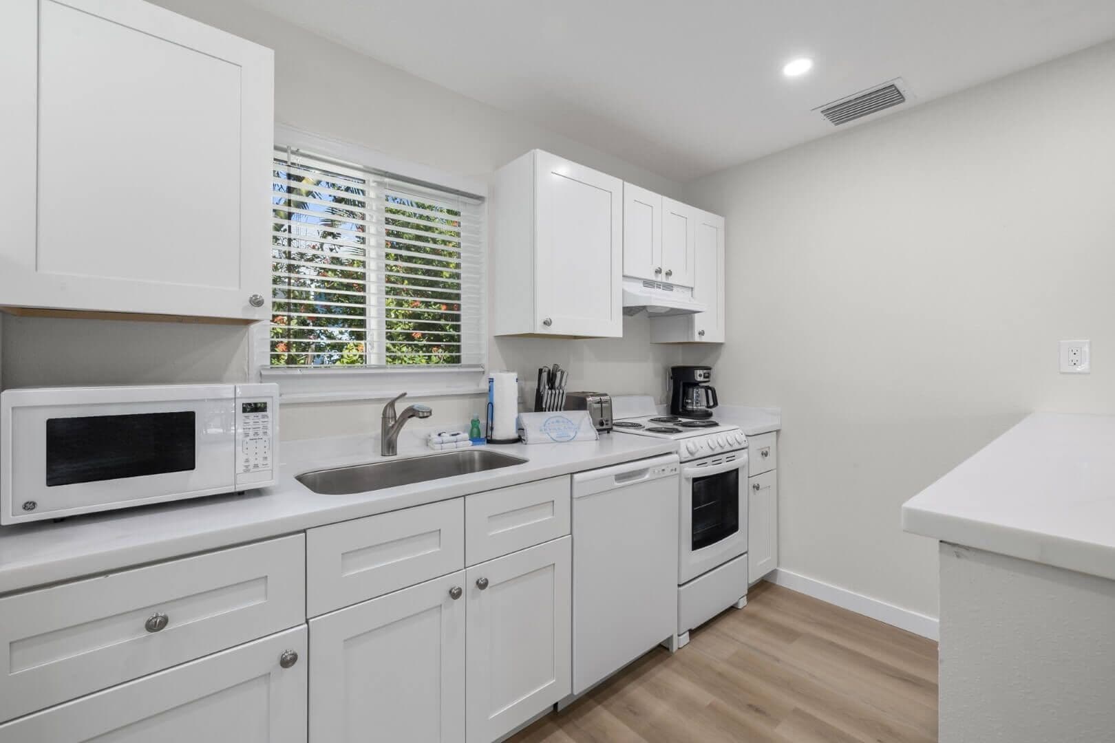 A modern kitchen with white cabinets, a microwave, a sink, a stove, and a coffee maker.