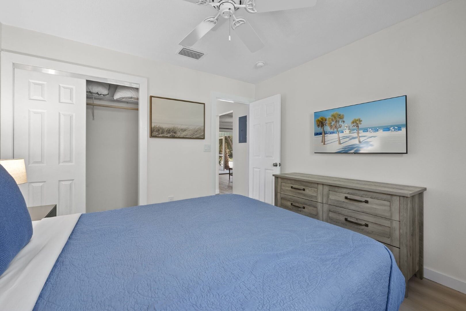 A bedroom with a bed, a dresser, a ceiling fan, a painting, and a closet.